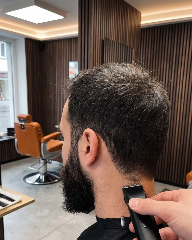 Vollbart von hinten seitlich, der Barber zieht mit dem Trimmer die Linie im Nacken nach